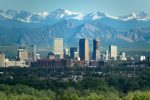 The snow covered Rocky Mountains and Indian Peaks rise over wind turbines, Boulder Flatirons and Downtown Denver skyscrapers, hotels, office and apartment buildings.